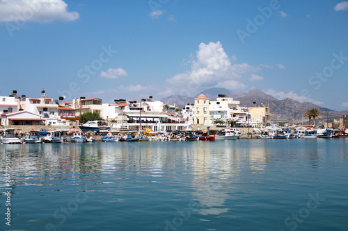 Typical traditional greek town by the sea. The Mediterranean coast of Crete, reflection of houses in the blue water on the clear blue sky background, summer landscape © Cheshka