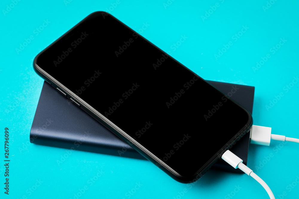 Smartphone charging with Power Bank via USB cable on blue background top view. Smartphone charging with Power Bank via USB cable on blue background top view.