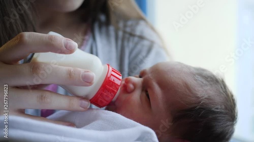 Young mother feeding her infant baby giving a nipple bottle of milk nutrition to her child daughter couple of days after birth photo