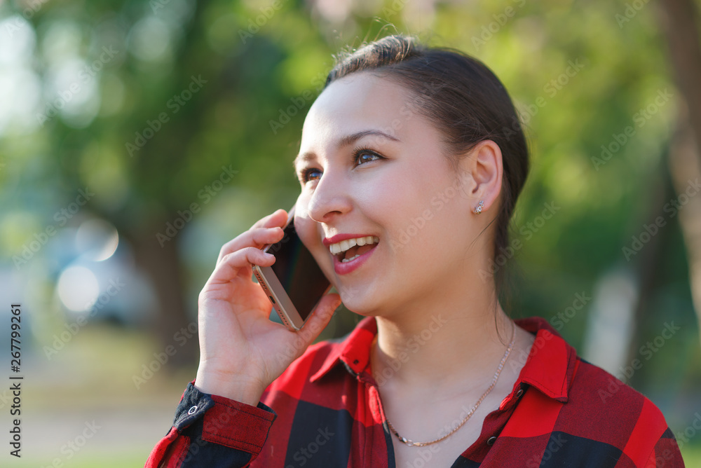 portrait of a happy young brunette girl with a smartphone in her hand, raised to her ear. Girl talking on mobile and smiling. shot on a Sunny day portrait of a happy young brunette girl with a smartphone in her hand, raised to her ear. Girl talking on mobile and smiling. shot on a Sunny day
