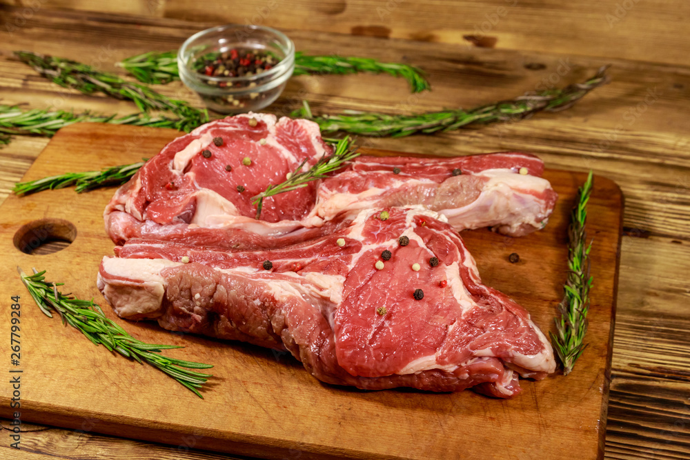 Raw fresh beef rib eye steaks on bone with spices and rosemary on wooden table