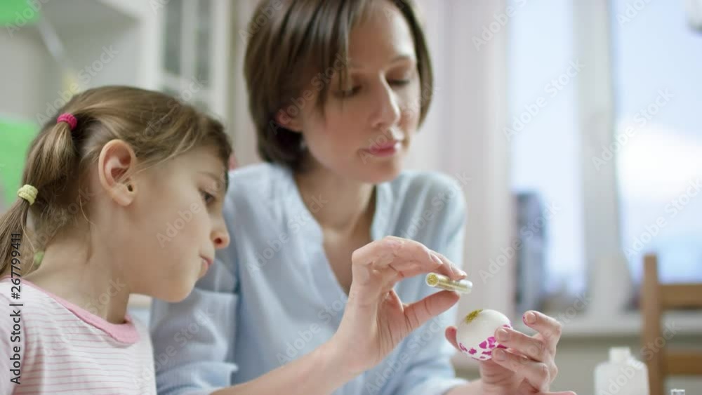 mother show her daughter how to decorate egg with sparkles for holiday with a brush