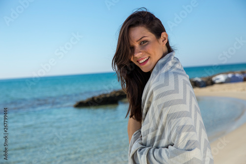 Pretty young girl wrapped in beach towel poses on camera with a smiling face. Portrait shot and wonderful hair. Beauty and summer concept. 