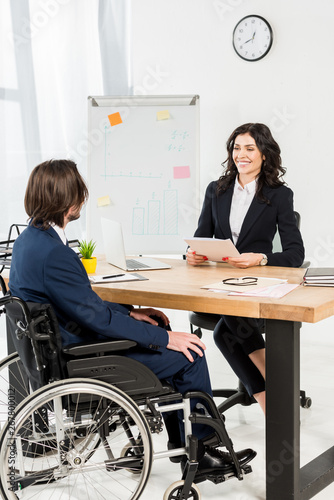 happy recruiter looking at disabled man while holding documents and smiling in office