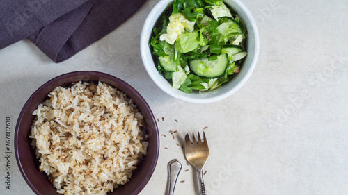 Bowl of rice with spices and vegetable salad on a gray background