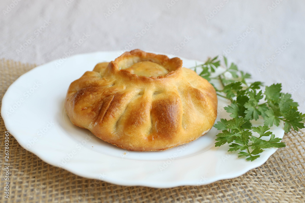 Traditional russian chicken pie kurnik on a plate laying on a table napkin on a grey background, side view, horizontal Traditional russian chicken pie kurnik on a plate laying on a table napkin on a grey background, side view, horizontal