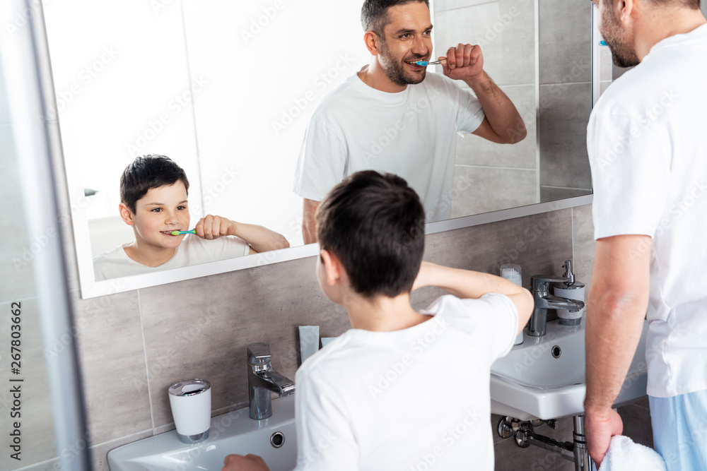 father and son brushing teeth in bathroom in morning father and son brushing teeth in bathroom in morning