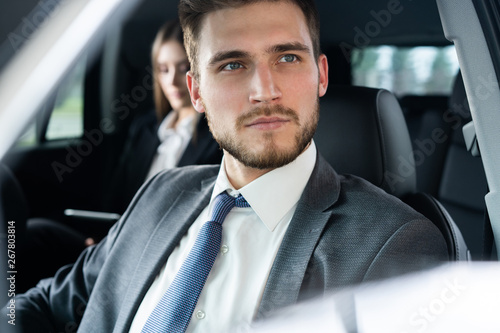 Success in motion. Handsome young man in full suit smiling while driving a car. © opolja