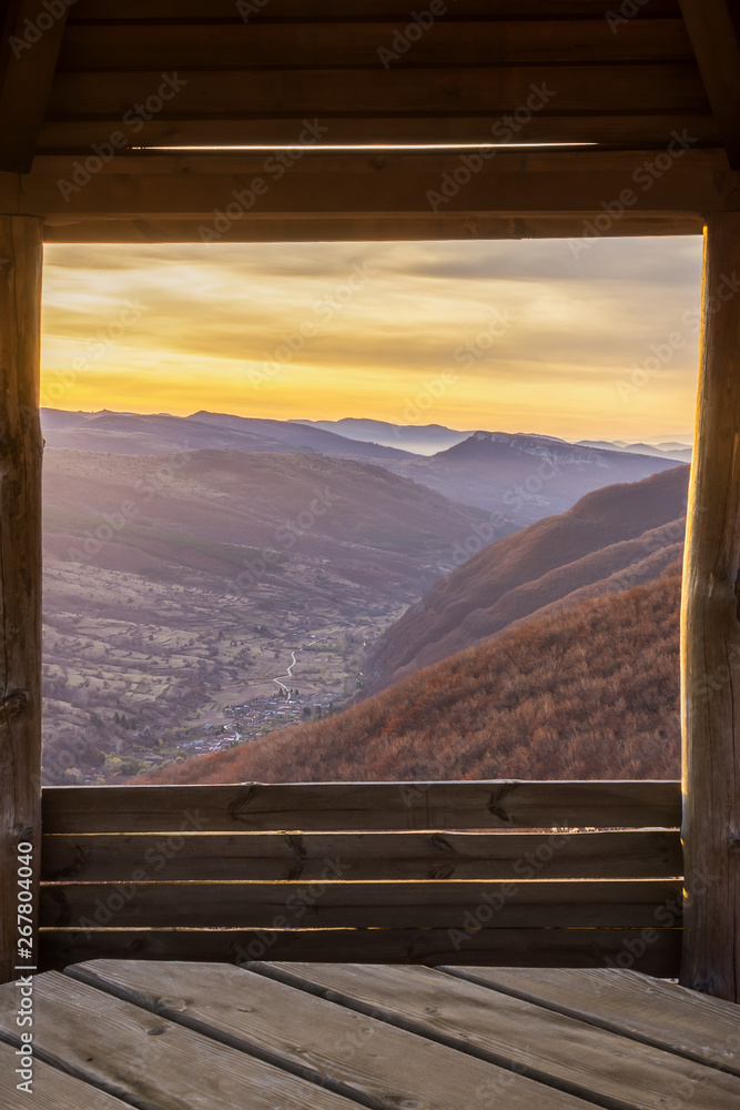 Framed view through the wooden summer house on a valley of village Dojkinci and beautiful sunrise in the mountains Framed view through the wooden summer house on a valley of village Dojkinci and beautiful sunrise in the mountains