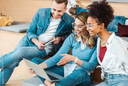 smiling multicultural students using laptop in lecture hall