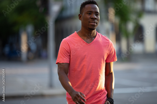 African american man in living coral t-shirt walking at city street, casual style, crossing a road © antgor