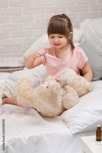 cute child girl playing doctor with teddy bear at home.