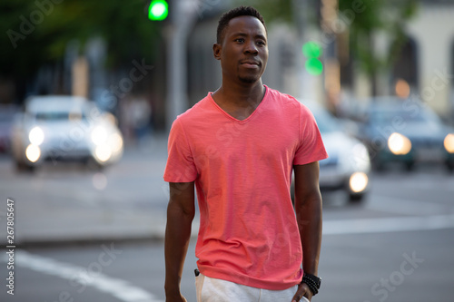 African american man in living coral t-shirt walking at city street, casual style, crossing a road