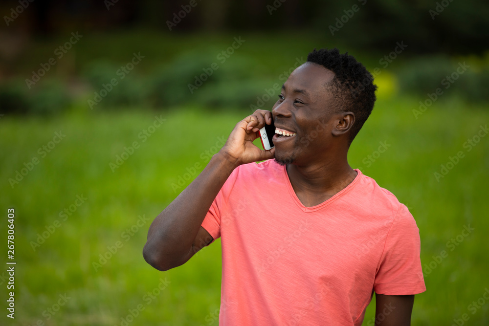 African american man in living coral t-shirt talking by smartphone at summer day African american man in living coral t-shirt talking by smartphone at summer day