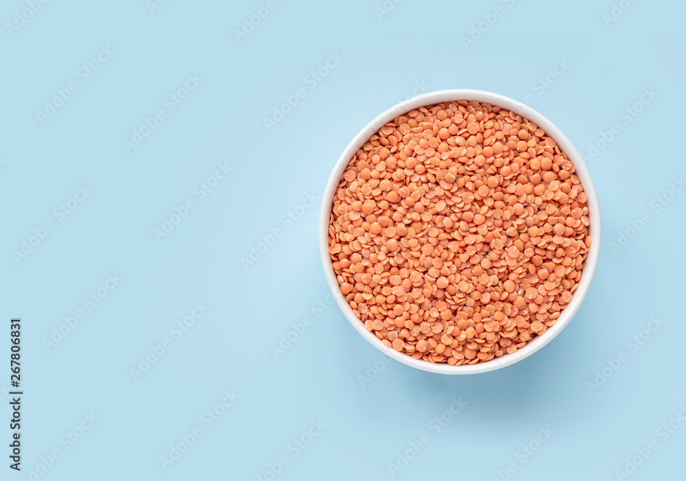 Raw red lentils in a white bowl on a blue background. Top view, copy space, minimalistic. Raw red lentils in a white bowl on a blue background. Top view, copy space, minimalistic.