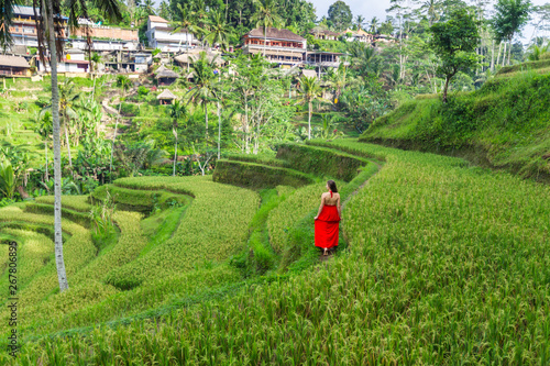 Woman in red dress admires rice fields Bali in Tegallalang. Rustic Ubud village landscape outside. Fashion style