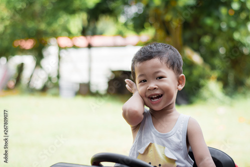 Little boy driving red car with the steering wheel. Little boy driving big toy car and having fun on grass outdoors.