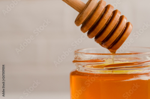 Polyfloral honey flows from a wooden honey spoon. A viscous stream of sweet amber flower honey flows from a wooden honey spoon into a glass jar.