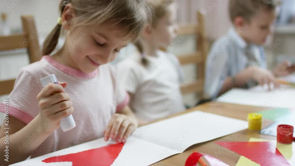 girl using glue stick for making her application for holiday decoration with brothers on background and talking with them girl using glue stick for making her application for holiday decoration with brothers on background and talking with them