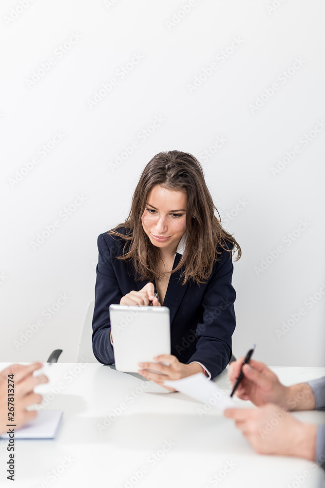 Young fashionable woman using tablet device while sitting at the desk on a business meeting. Young fashionable woman using tablet device while sitting at the desk on a business meeting.