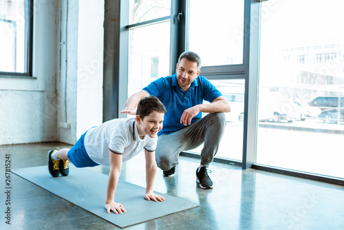 father helping son with push up exercise at gym with copy space