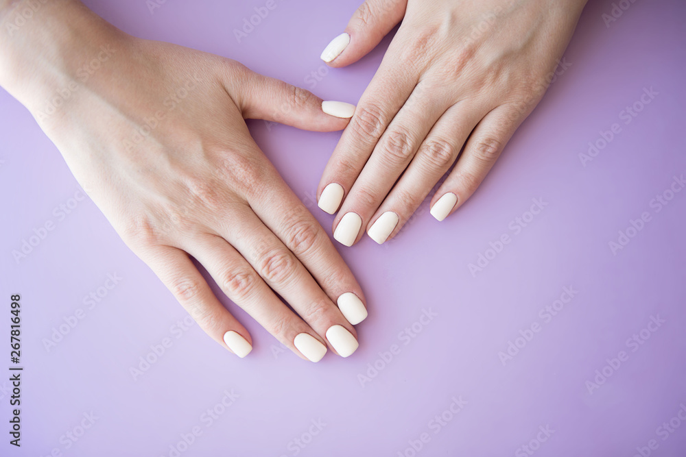 Manicured hands on purple background. Hands with manicured nails colored with beige nail polish. Manicured hands on purple background. Hands with manicured nails colored with beige nail polish.