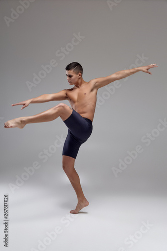 Photo of a handsome man ballet dancer, dressed in a black shorts, making a dance element against a gray background in studio.