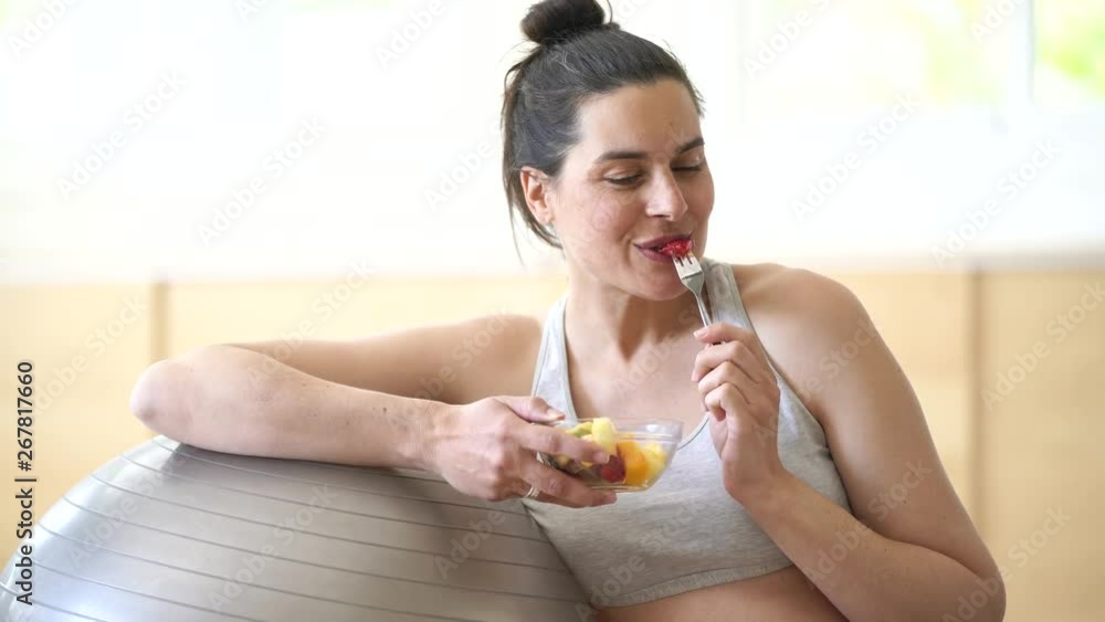 Fitness pregnant woman eating fruit salad by fitness ball Fitness pregnant woman eating fruit salad by fitness ball