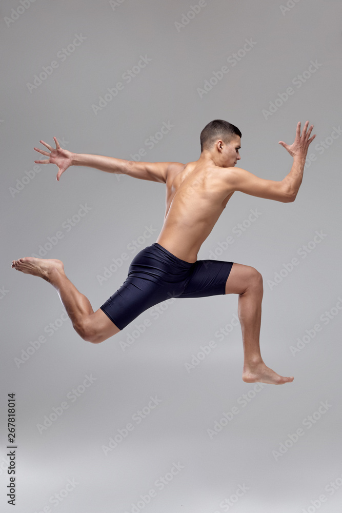 Photo of a handsome man ballet dancer, dressed in a black shorts, making a dance element against a gray background in studio.