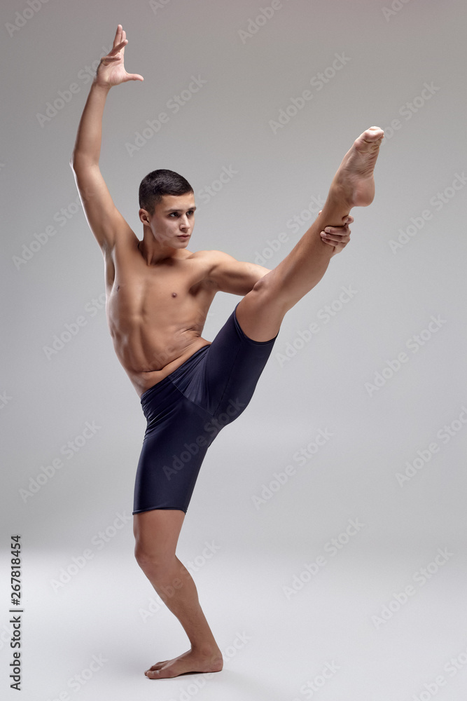 Obraz premium Photo of a handsome man ballet dancer, dressed in a black shorts, making a dance element against a gray background in studio.