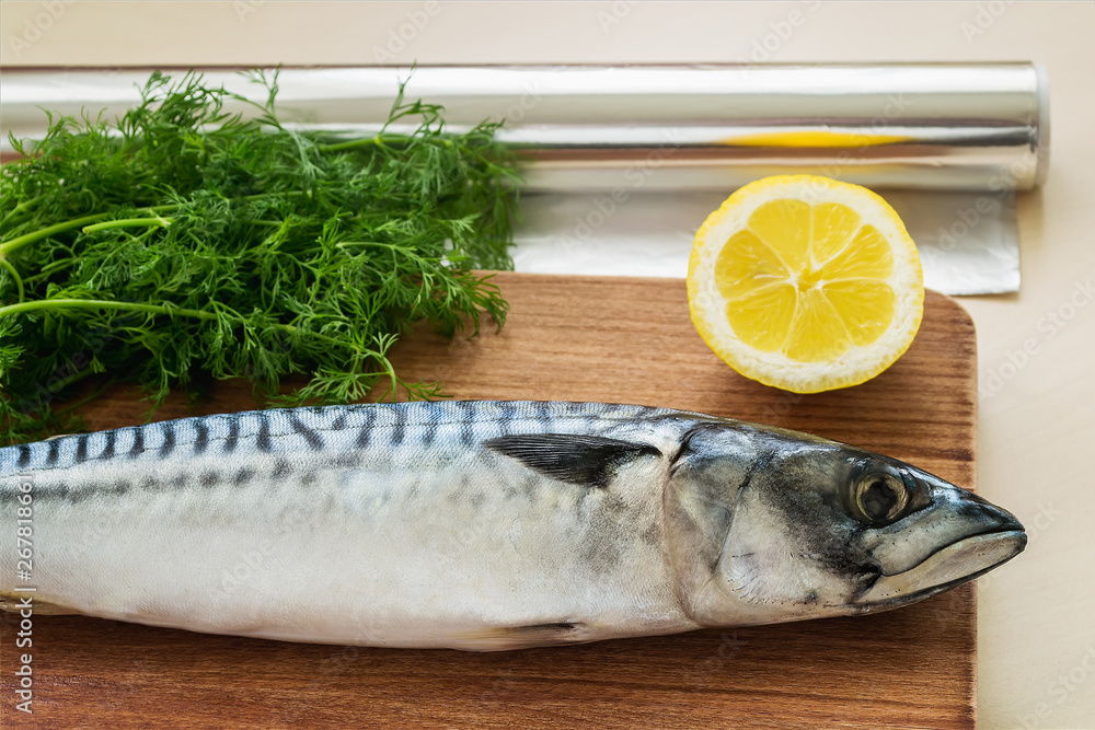 Roll of aluminum foil and one raw mackerel, dill and lemon on a brown wooden cutting board. Seafood, healthy eating and cook at home. Roll of aluminum foil and one raw mackerel, dill and lemon on a brown wooden cutting board. Seafood, healthy eating and cook at home.