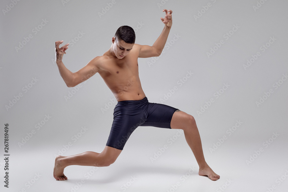 Fototapeta premium Photo of a handsome man ballet dancer, dressed in a black shorts, making a dance element against a gray background in studio.