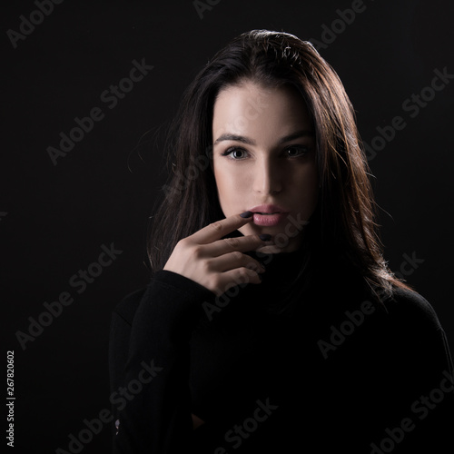 Beautiful girl posing over black background. Young pretty woman in studio.