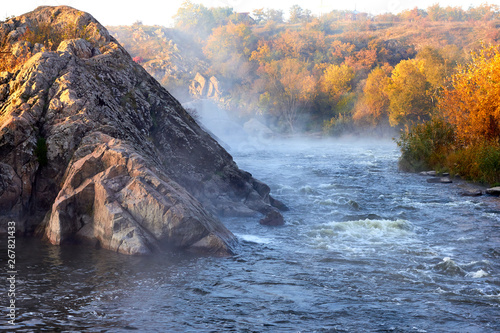 Morning haze over the water of the wild mountain river with rapids. Autumn morning landscape of the river