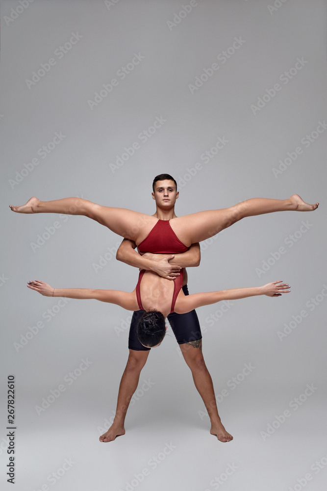 Obraz premium The couple of an athletic modern ballet dancers are posing against a gray studio background.