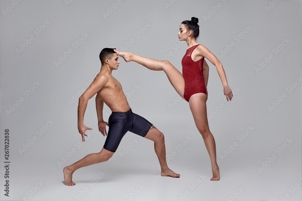 The couple of an athletic modern ballet dancers are posing against a gray studio background. The couple of an athletic modern ballet dancers are posing against a gray studio background.