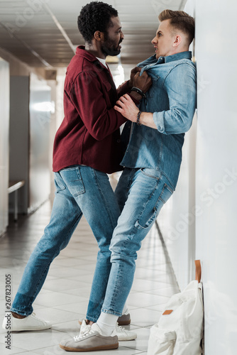 full length view of two students in jeans fighting in corridor in college photo