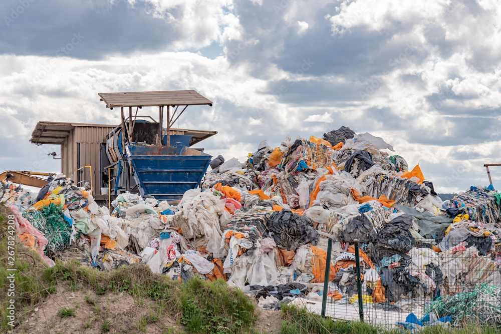 Garbage dump with many colorful garbage, cloudy sky.