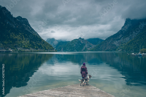 Kobieta z psem Springer Spanielem stoją na drewnianym pomoście nad górskim jeziorem Traunsee w Austrii w pochmurny dzień © Tomasz