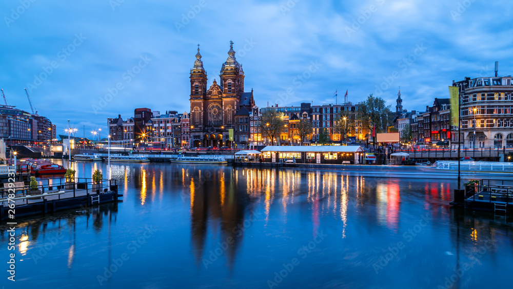 Obraz premium Scenic night view of Basilica of Saint Nicholas and skyline of the the old city district reflected in the water of the canal. Blue hours, Amsterdam, Netherlands.
