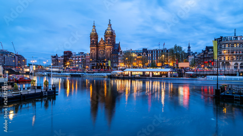 Scenic night view of Basilica of Saint Nicholas and skyline of the the old city district reflected in the water of the canal. Blue hours, Amsterdam, Netherlands.