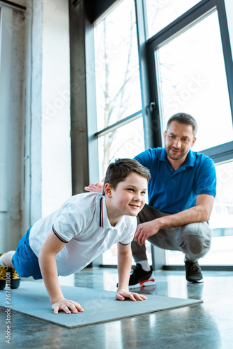 father helping son with push up exercise at gym