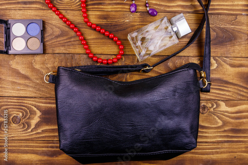 Women accessories on wooden background. Clutch bag, bottle of perfume, eye shadow, necklace and earrings on wood table. Beauty and fashion composition. Top view, flat lay