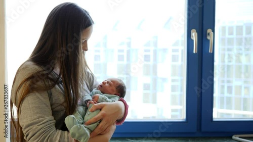 Young mother holding her infant baby daughter in maternity hospital room couple of days after birth photo