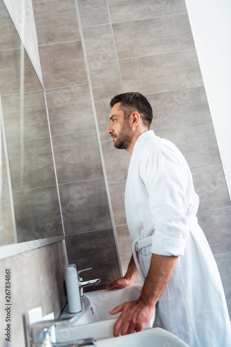 handsome man in bathrobe looking at mirror in bathroom during morning routine © LIGHTFIELD STUDIOS