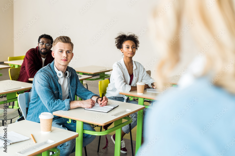 multiethnic students sitting at desks and looking at teacher multiethnic students sitting at desks and looking at teacher