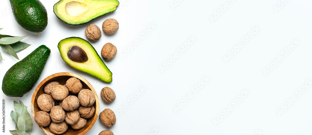Ripe fresh avocado, walnuts in wooden bowl, eucalyptus twigs on white background top view Flat lay copy space. Fruits Healthy food concept, diet, healthy lifestyle. - obrazy, fototapety, plakaty 