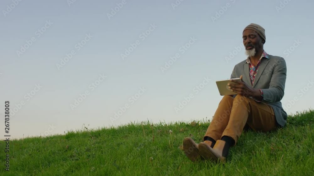 Camera reveals a senior man drawing using a digital tablet out in the countryside Camera reveals a senior man drawing using a digital tablet out in the countryside