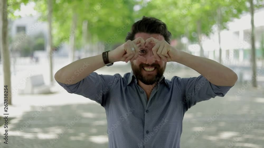 Happy man showing hand heart symbol outdoor. Handsome bearded man showing hand heart gesture and smiling at camera on street. Gesturing concept Happy man showing hand heart symbol outdoor. Handsome bearded man showing hand heart gesture and smiling at camera on street. Gesturing concept