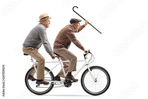 Two elderly men riding a tandem bicycle and waving with a walking cane